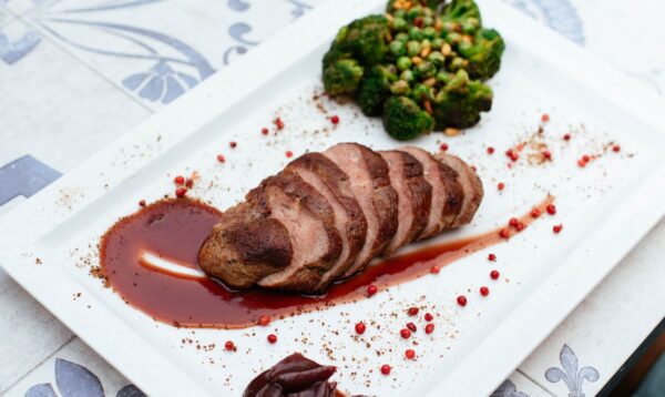 Deliciously plated duck breast with broccoli and sauce on a white plate.